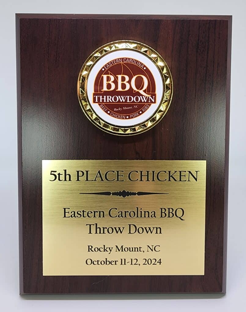 A wooden recognition plaque featuring a circular emblem labeled &quot;Eastern Carolina BBQ Throwdown.&quot; Below the emblem, a gold plate is engraved with &quot;5th PLACE CHICKEN,&quot; followed by &quot;Eastern Carolina BBQ Throw Down, Rocky Mount, NC, October 11-12, 2024.&quot;