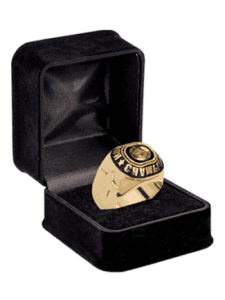 A gold championship sports ring displayed in an open black velvet box, featuring engraved text and design details on the band and face.
