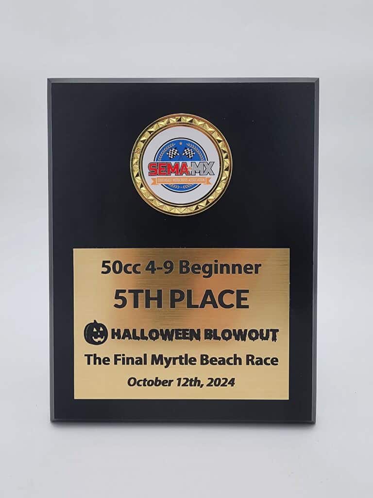 A black plaque featuring a gold medal emblem with a logo and text below that reads &quot;50cc 4-9 Beginner, 5th PLACE, HALLOWEEN BLOWOUT, The Final Myrtle Beach Race, October 12th, 2024.&quot;