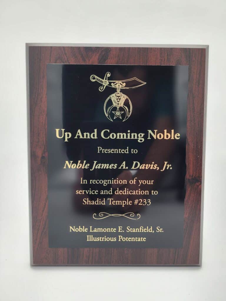 A wooden recognition plaque with gold text and a decorative emblem, awarded to Noble James A. Davis, Jr. for service and dedication to Shadid Temple #233, presented by Noble Lamonte E. Stanfield, Sr.