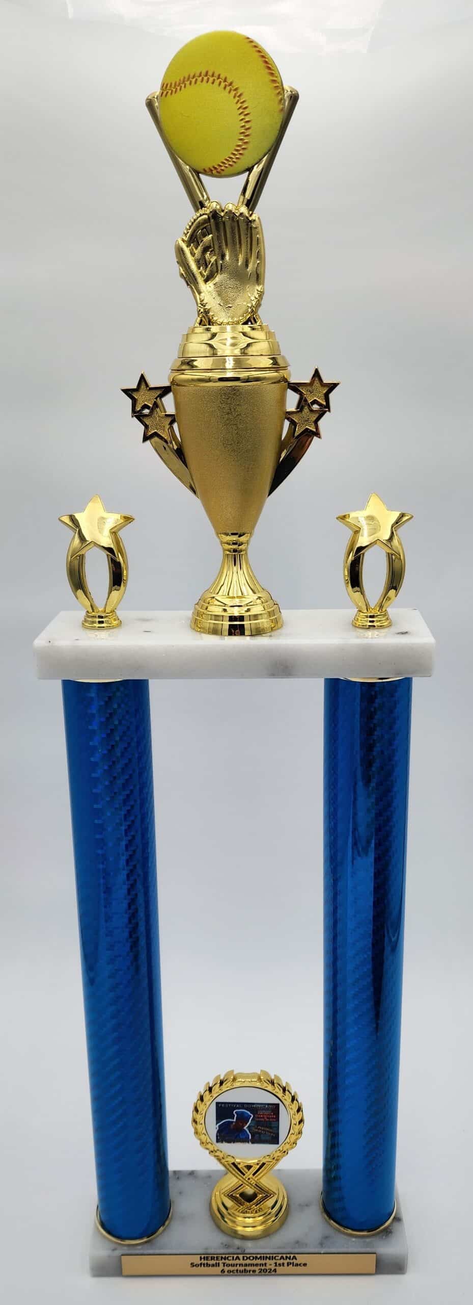 A sports trophy featuring two tall blue columns supporting a golden cup with star accents and a softball on top, labeled "HERENCIA DOMINICANA Softball Tournament - 1st Place, 6 octubre 2024."