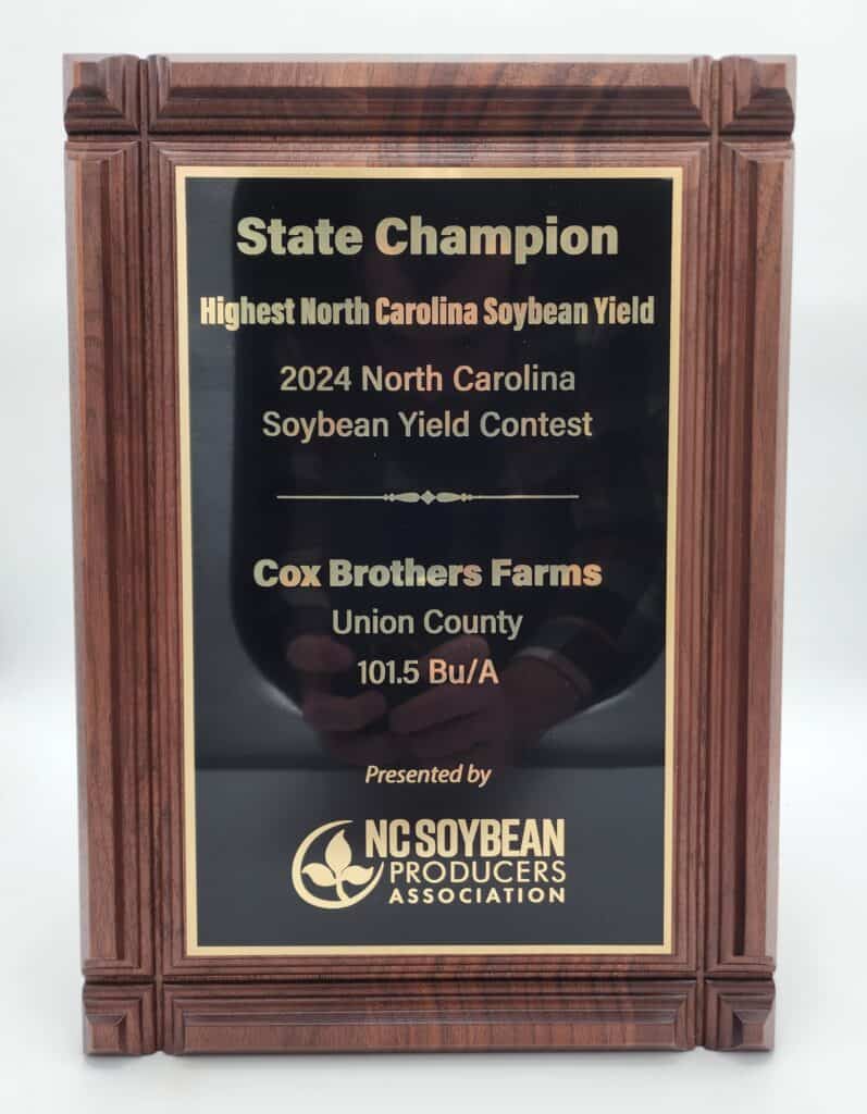A wooden plaque with a black and gold plate, awarded to Cox Brothers Farms for the highest North Carolina soybean yield in the 2024 North Carolina Soybean Yield Contest, presented by the NC Soybean Producers Association.