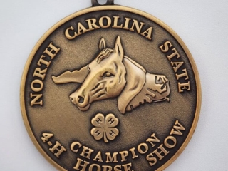 A bronze medal featuring an embossed horse's head at the center, surrounded by the text 'North Carolina State 4-H Champion Horse Show.' A four-leaf clover symbol with '4-H' text is also embossed below the horse's head.