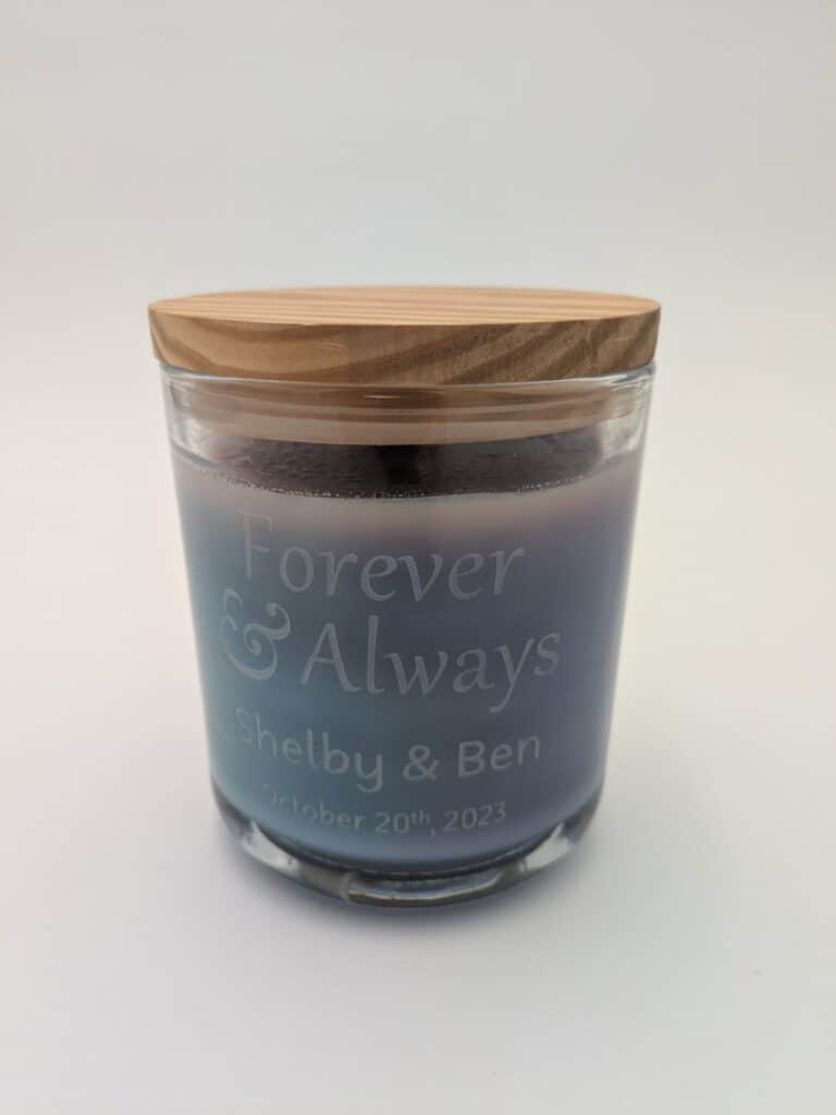 A small glass candle with a wooden lid, engraved with 'Forever &amp; Always, Shelby &amp; Ben, October 20th, 2023.'