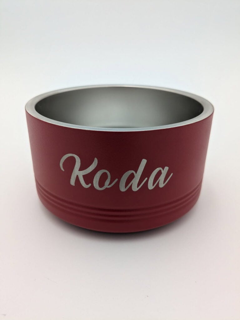 A red pet bowl with the name "Koda" engraved on it in silver lettering, featuring a smooth metallic interior.