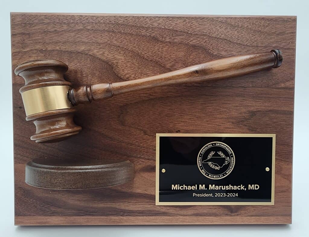 A wooden plaque with a gavel mounted on it and a black nameplate reading "Michael M. Marushack, MD, President, 2023-2024" next to a logo.
