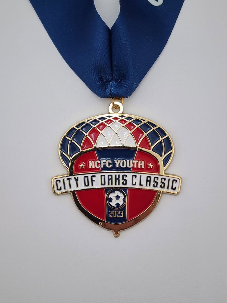 A custom medal featuring the design "NCFC Youth City of Oaks Classic" with a soccer theme, set against a navy, red, and white background, and attached to a blue ribbon.