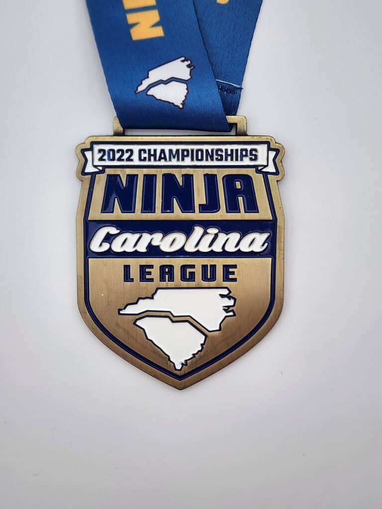 A custom medal for the 2022 Championships of the Ninja Carolina League, featuring a design with the text and an outline of North and South Carolina on a blue ribbon.