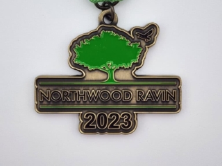 A custom medal with a green and silver design, featuring a tree and a bird silhouette, inscribed with 'Northwood Ravin 2023' and attached to a green and white ribbon.