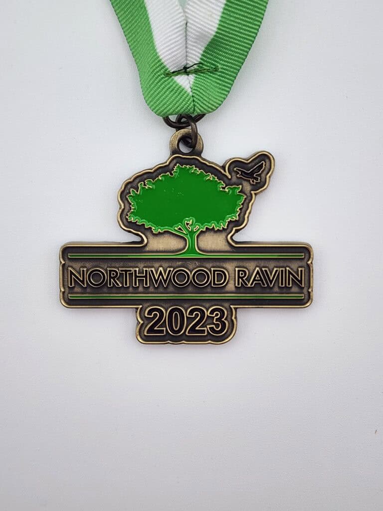 A custom medal with a green and silver design, featuring a tree and a bird silhouette, inscribed with 'Northwood Ravin 2023' and attached to a green and white ribbon.