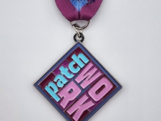 A diamond-shaped custom medal with the words 'Patch Work' in bold, colorful letters, attached to a purple ribbon with a blue stripe.