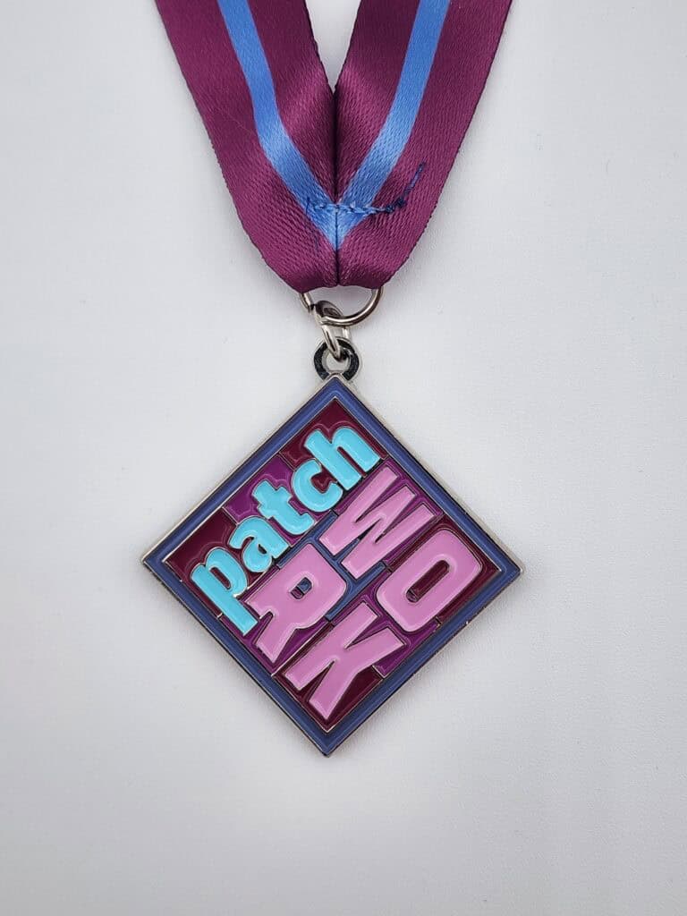 A diamond-shaped custom medal with the words 'Patch Work' in bold, colorful letters, attached to a purple ribbon with a blue stripe.