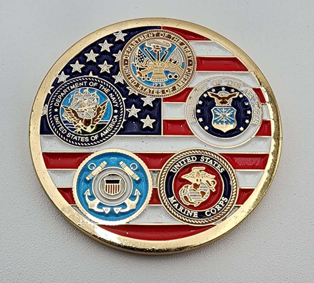A commemorative coin featuring the emblems of the United States Army, Navy, Air Force, Marine Corps, and Coast Guard on a background resembling the American flag, with a gold border.