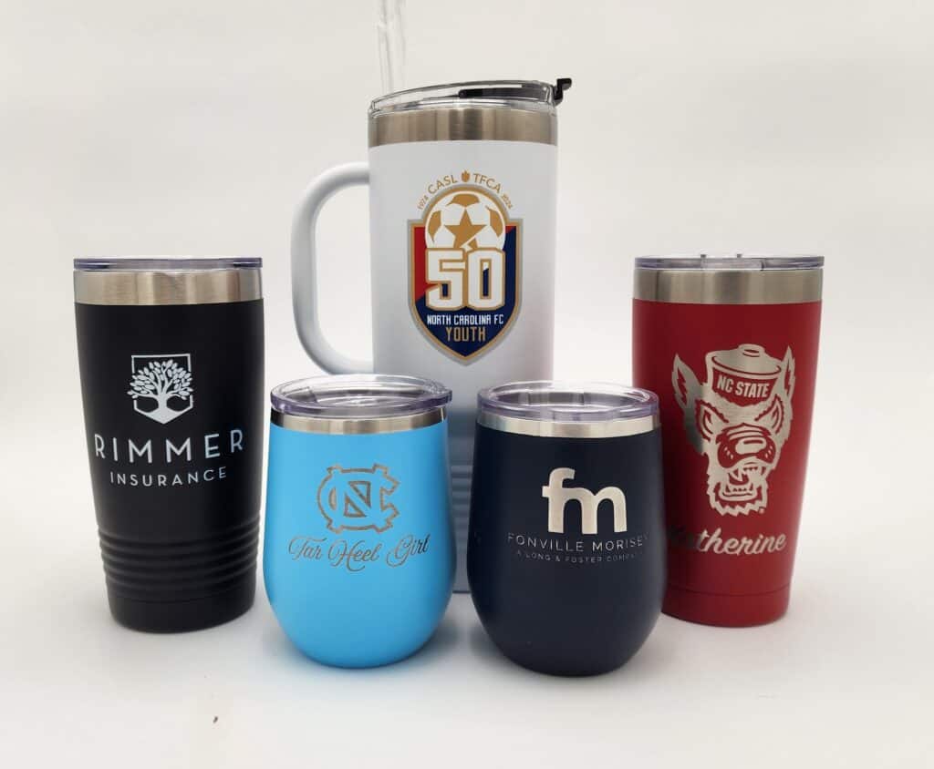A collection of five branded tumblers and mugs featuring different logos and designs, including "Rimmer Insurance," "Tar Heel Girl," and "NC State." They are displayed in a group with various colors and lid styles.