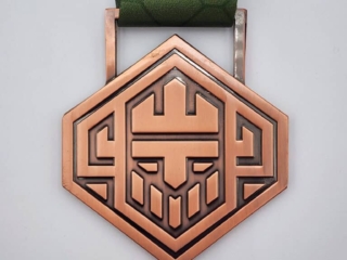 A custom hexagonal bronze medal featuring an abstract geometric design and attached to a green patterned ribbon.