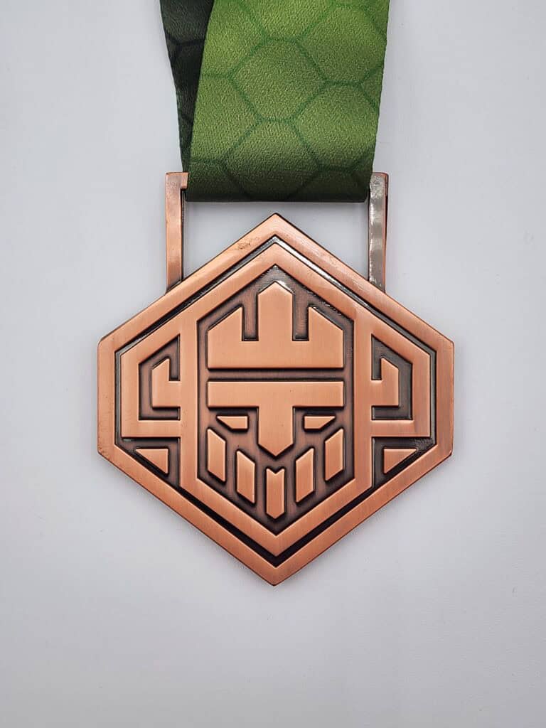 A custom hexagonal bronze medal featuring an abstract geometric design and attached to a green patterned ribbon.