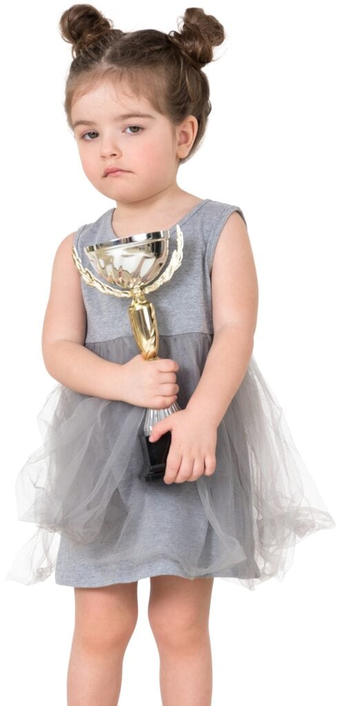 a little girl in a gray dress holding a trophy